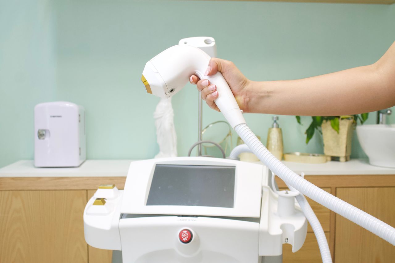 services-01 Close-up of a hand holding a laser hair removal device in a clinic setting.